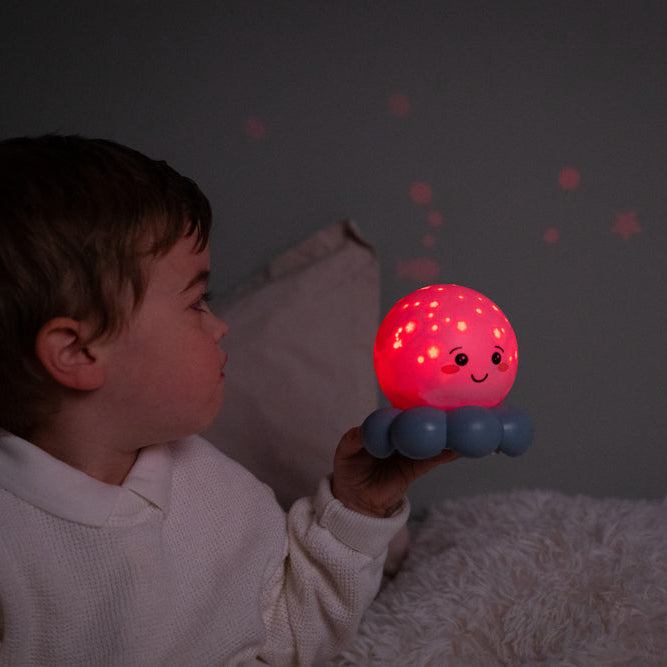 Child holding a glowing red night light with a smiling face in a dark room.