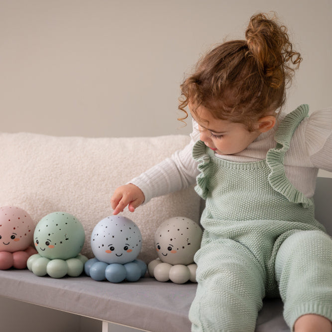 Child in a light green outfit playing with soft toys on a bench.