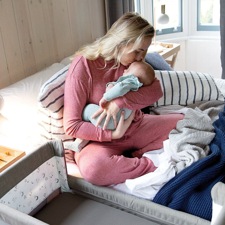 Woman in pink pajamas holding a baby in a crib with a blue blanket.