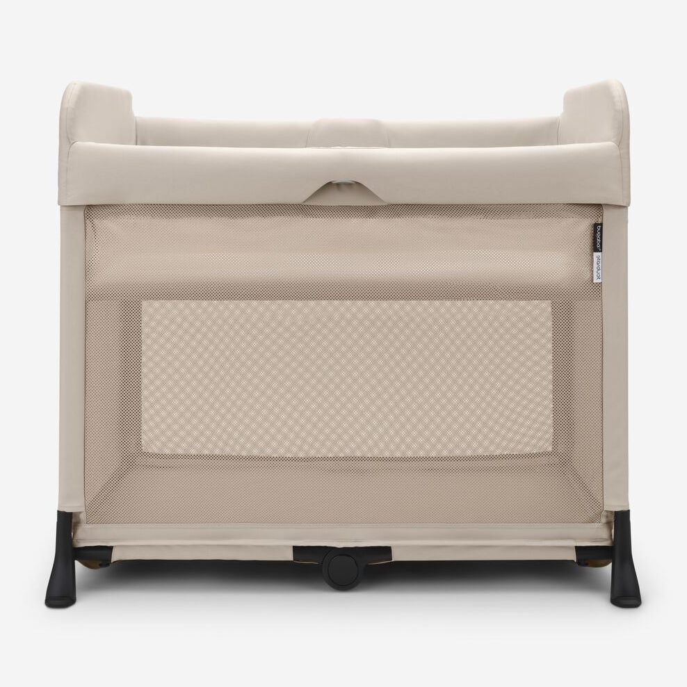 A portable baby playpen in a warm beige fabric with black wheels and feet, shown from the front against a light gray background.