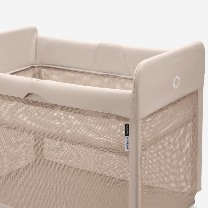 Beige baby crib with mesh sides on a white background