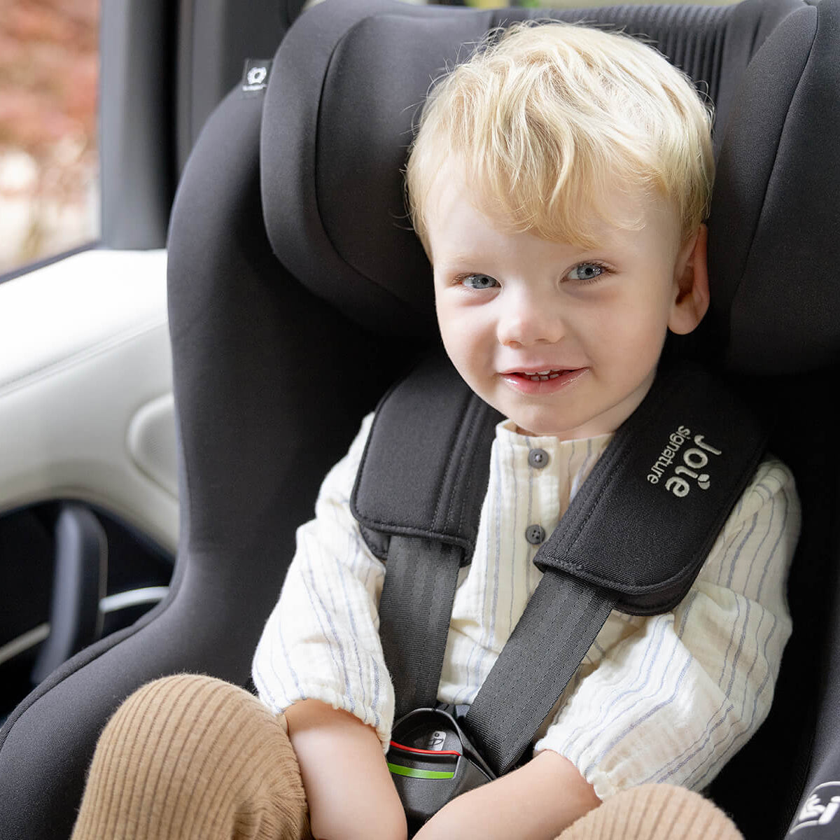 Child sitting in a car seat with a visible brand logo, inside a vehicle.