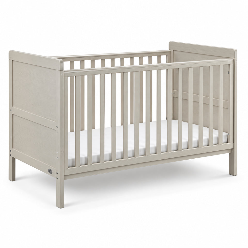 A light beige wooden convertible crib with vertical slats and a white mattress, shown from a three-quarter angle on a white background.