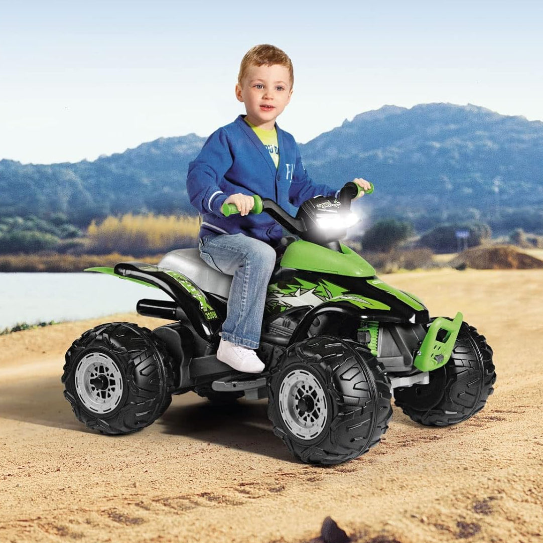 Child sitting on a green toy ATV in a natural setting with mountains and water in the background