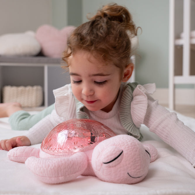 Child playing with a pink plush toy and glowing ball in a bedroom setting