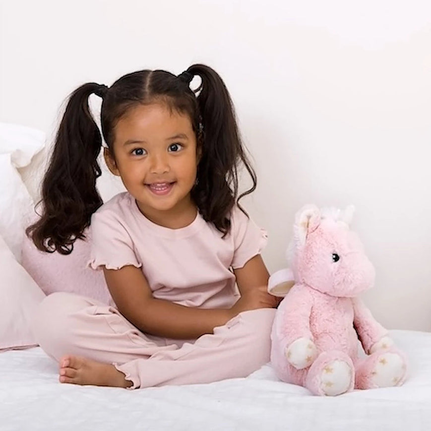 Young girl sitting on a bed with a pink unicorn plush toy, promotional text overlay.