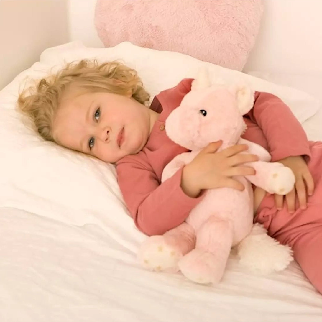 Child in pink pajamas lying on a bed with a pink teddy bear