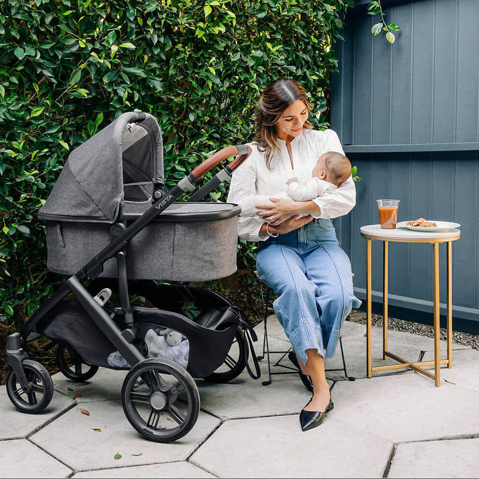 Woman holding a baby next to a stroller outdoors