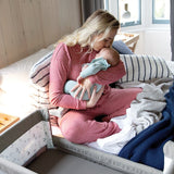 Woman in pink pajamas holding a baby in a crib with a blue blanket.