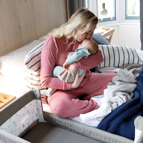 Woman in pink pajamas holding a baby in a crib with a blue blanket.