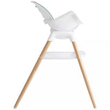A modern high chair with a white molded plastic seat and tray, supported by four natural light wood legs, shown from a side profile on a solid white background.