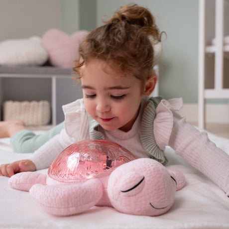 Child playing with a pink plush toy and glowing ball in a bedroom setting