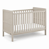 A light beige wooden convertible crib with vertical slats and a white mattress, shown on a clean white background.
