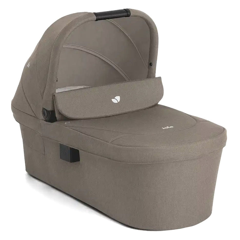 A baby travel seat in a taupe fabric, featuring a padded bassinet cover with a small white logo, a side release latch, and a black handle, shown on a white background.