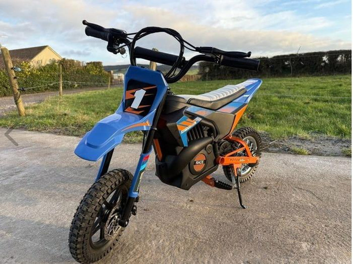 Children's blue and orange dirt bike on a concrete surface with a grassy field in the background.