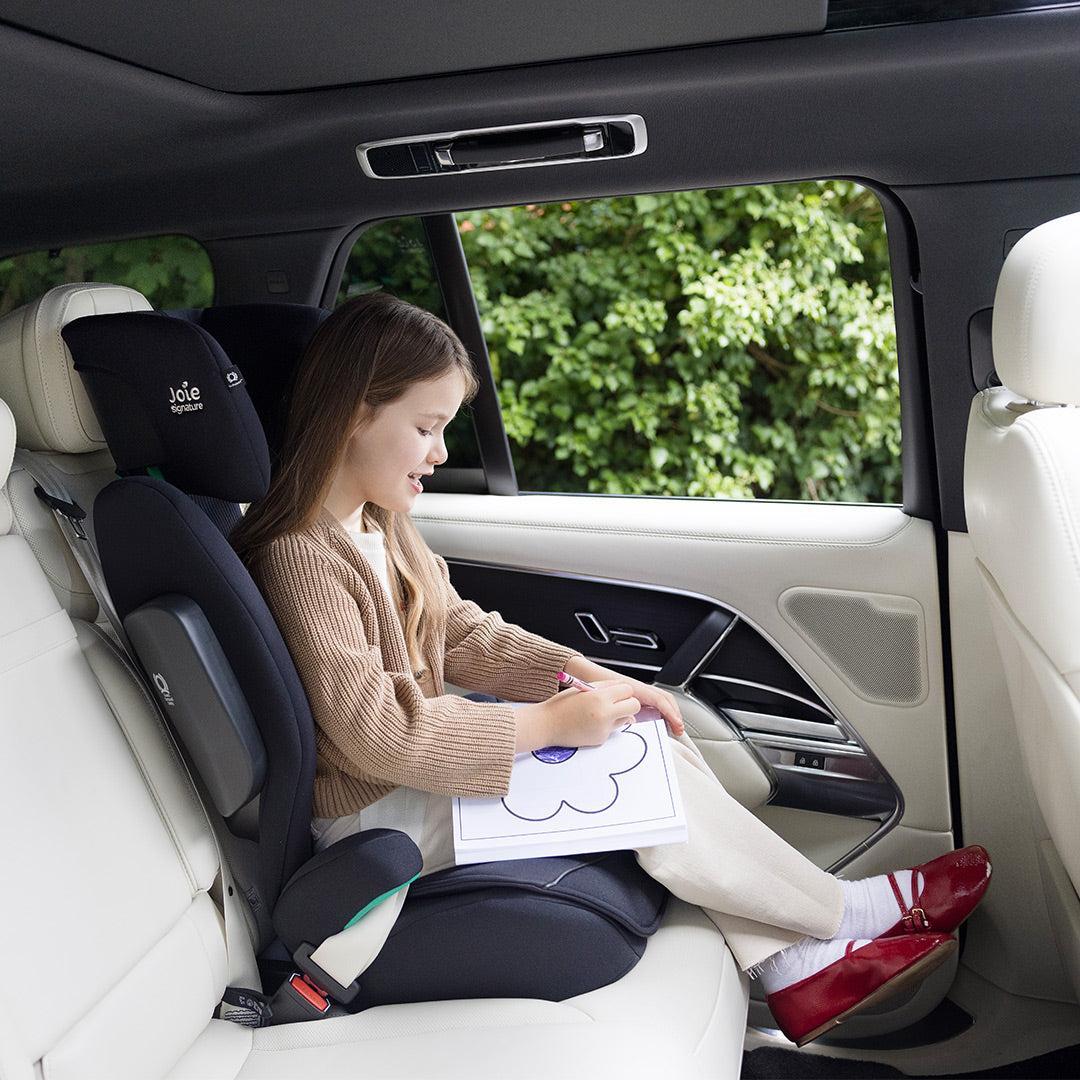 Child sitting in a car seat inside a vehicle, holding a coloring book.