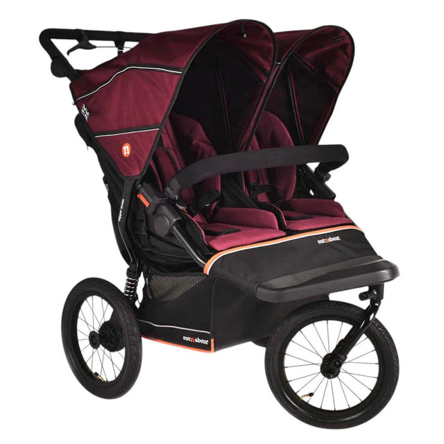 A double stroller travel system in burgundy and black, featuring a large canopy, two seats with harnesses, a footmuff, and a handlebar, shown on a plain white background.