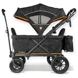 A black stroller wagon with orange accents, featuring a large black canopy, four wheels, and a side storage pocket, shown on a white background.
