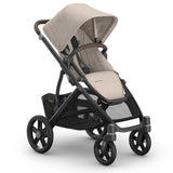 A premium stroller with a light beige fabric canopy and seat liner, paired with a dark gray frame and black wheels, shown on a clean white background.