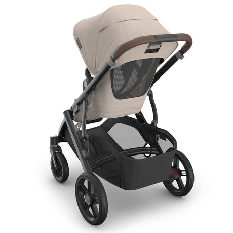 A stroller with a light beige fabric canopy and seat liner, a black frame, and black wheels, shown from a three-quarters rear angle on a white background.