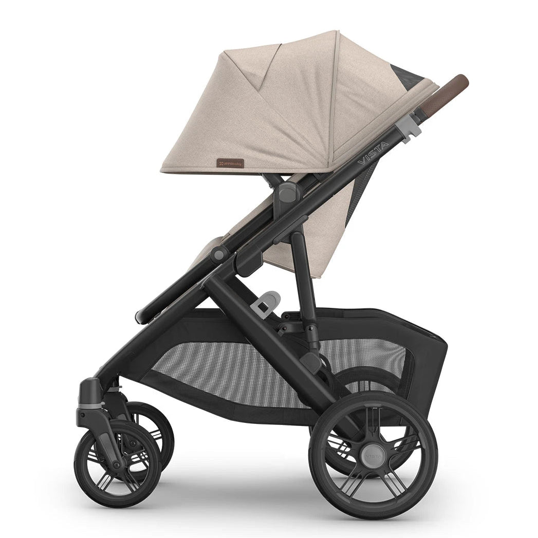 A side profile view of a stroller with a light beige fabric canopy and seat liner, a dark gray frame, and black wheels, set against a plain white background.